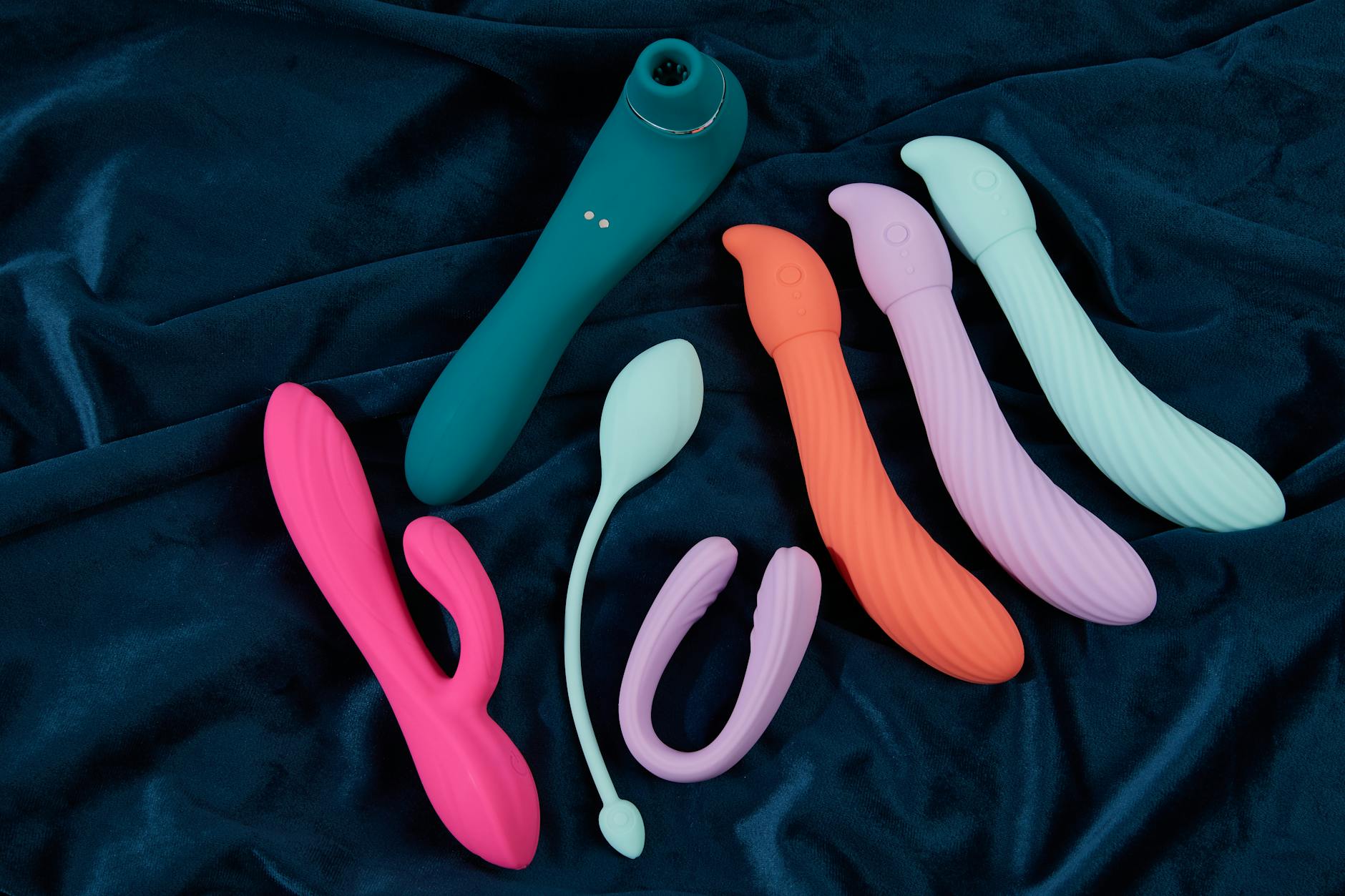 Colorful silicone clitoral vibrators arranged on dark fabric, showing various toy textures
