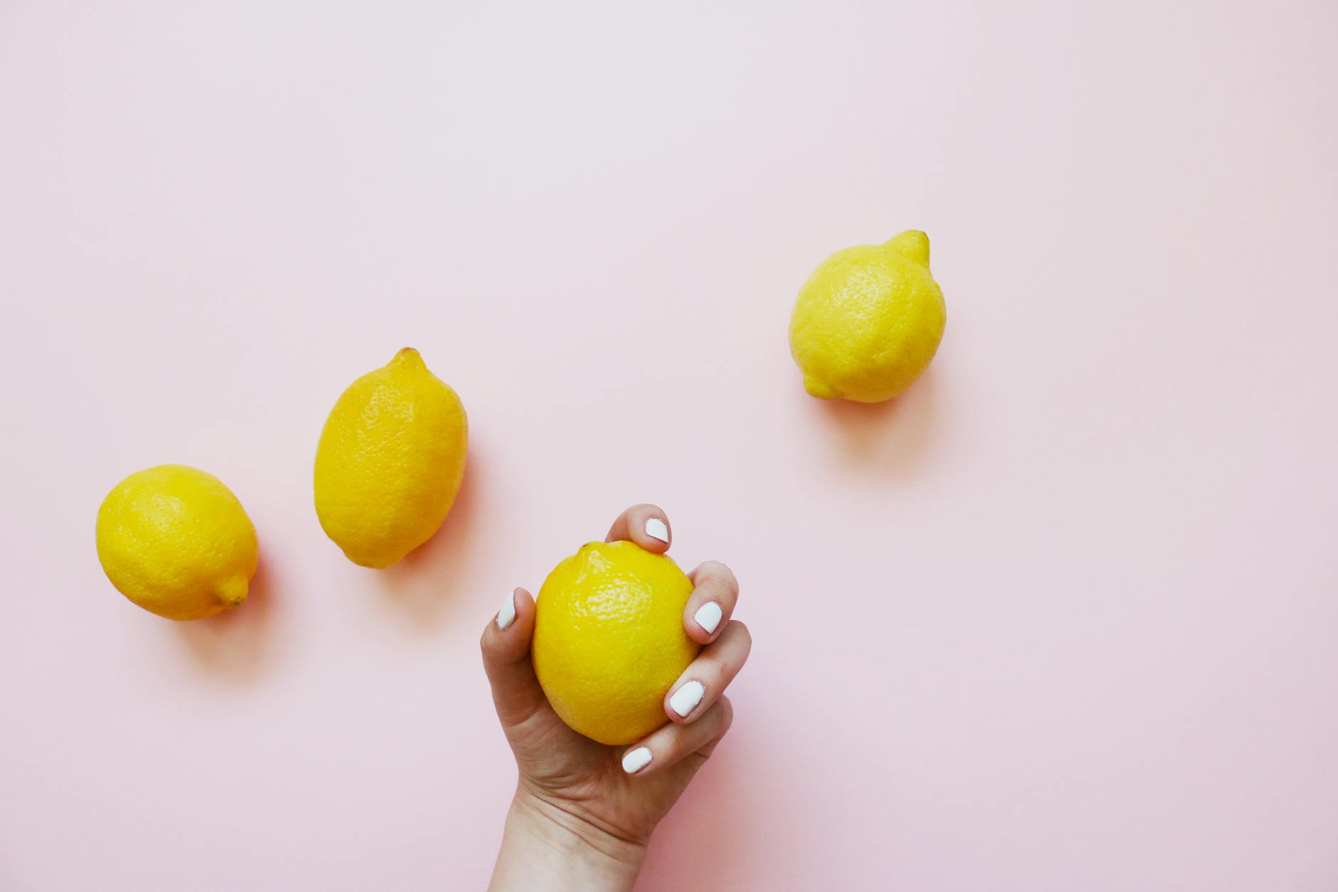 A lemon held in hand on a soft pink background, symbolizing gentle clitoral stimulation