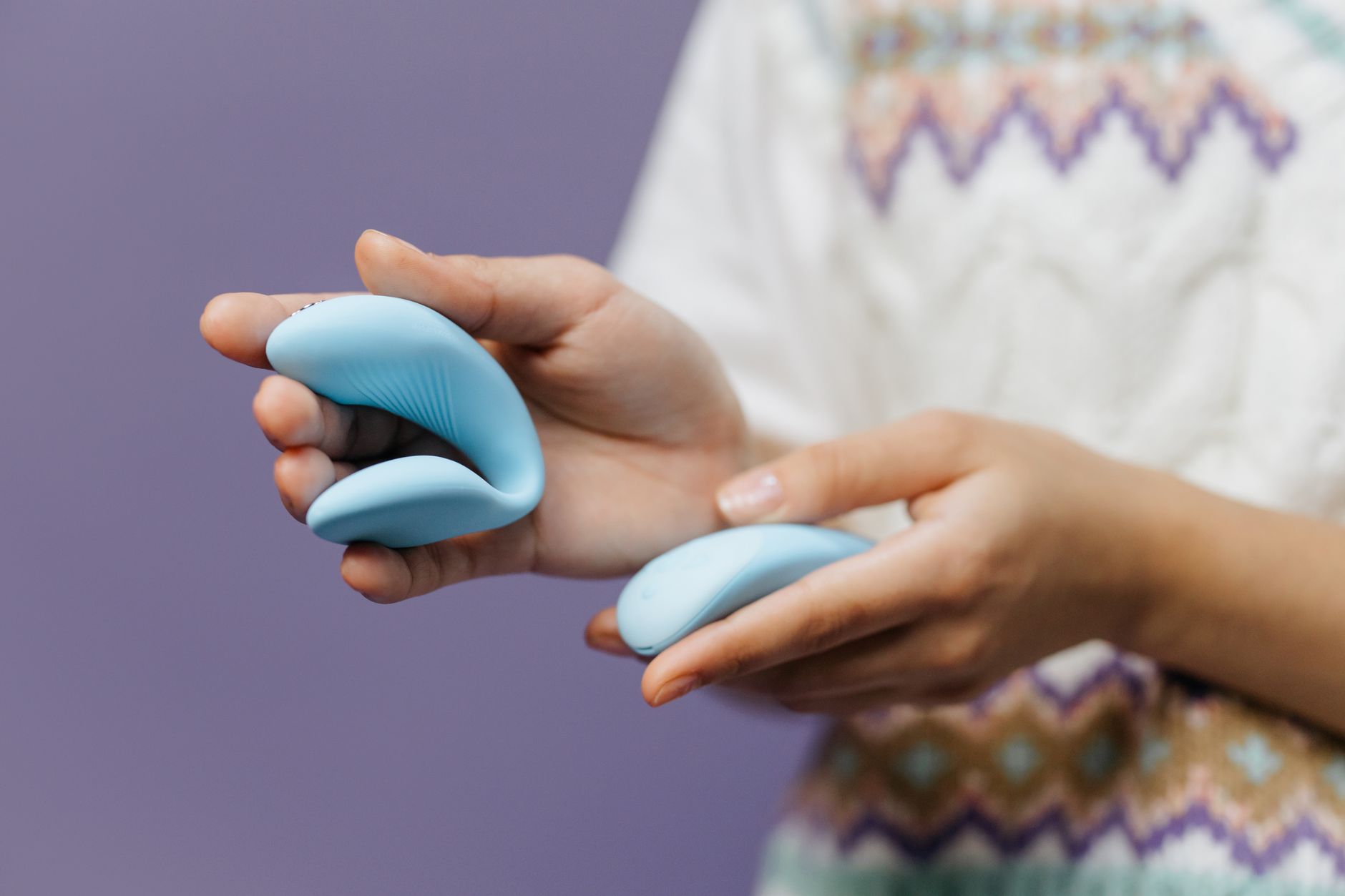 Hands holding a blue lemon suction vibrator against a purple background, demonstrating gentle clitoral stimulation.