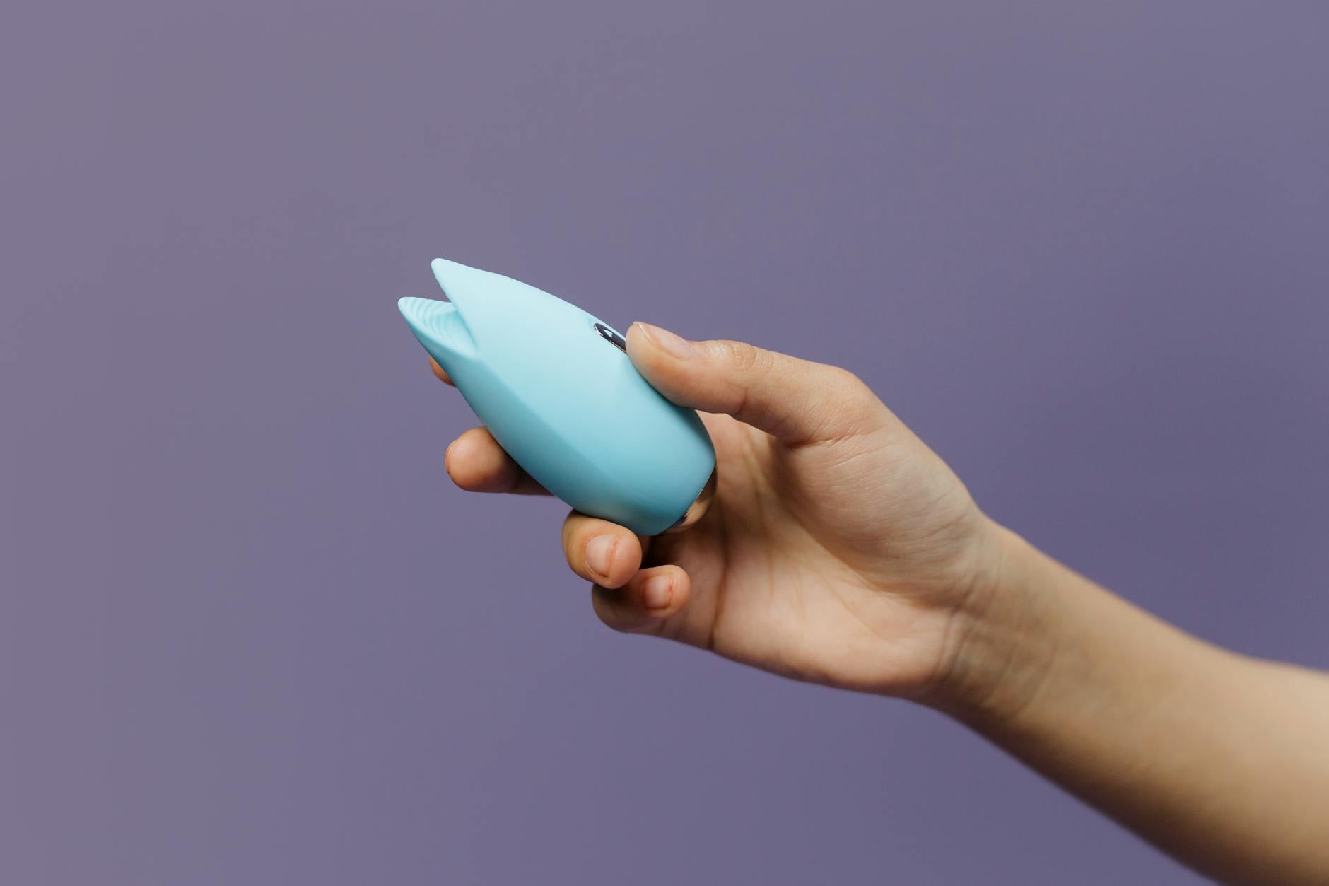 A hand reaching over a variety of colorful sex toys arranged on a table